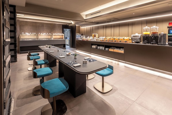 A modern bar area with a long counter, multiple stools, and a variety of beverages and food items.