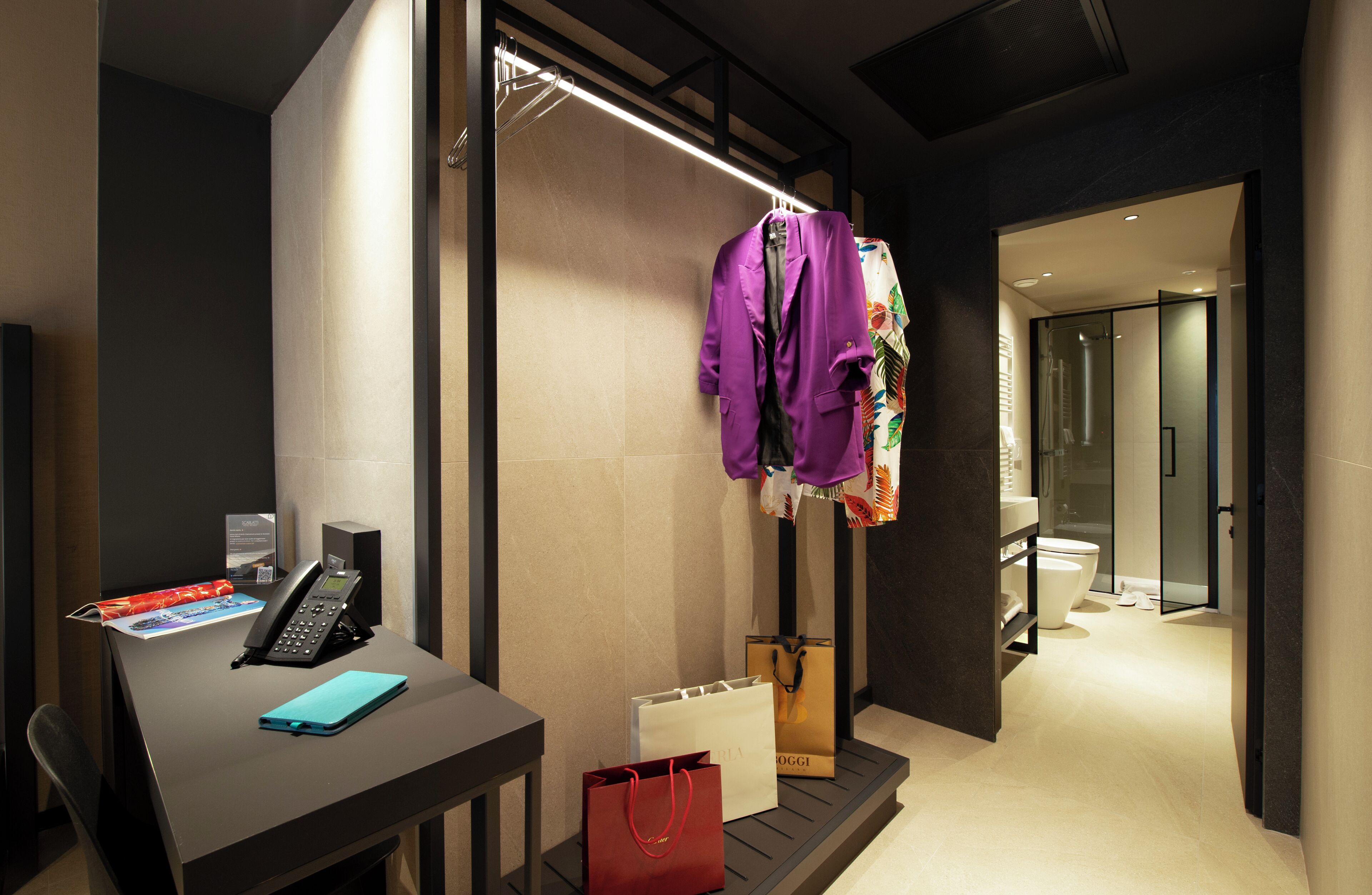 Una habitación de hotel moderna con un escritorio, teléfono y una bolsa de compras roja.