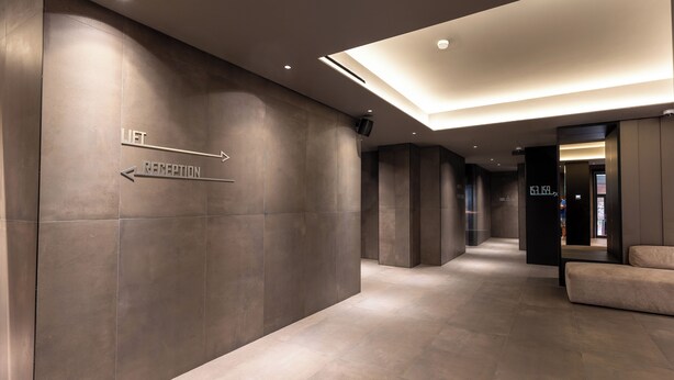A modern hotel corridor with directional signs to the lift and reception, a digital display, and a seating area. - Scarlatti Hotel Milano (Milan)