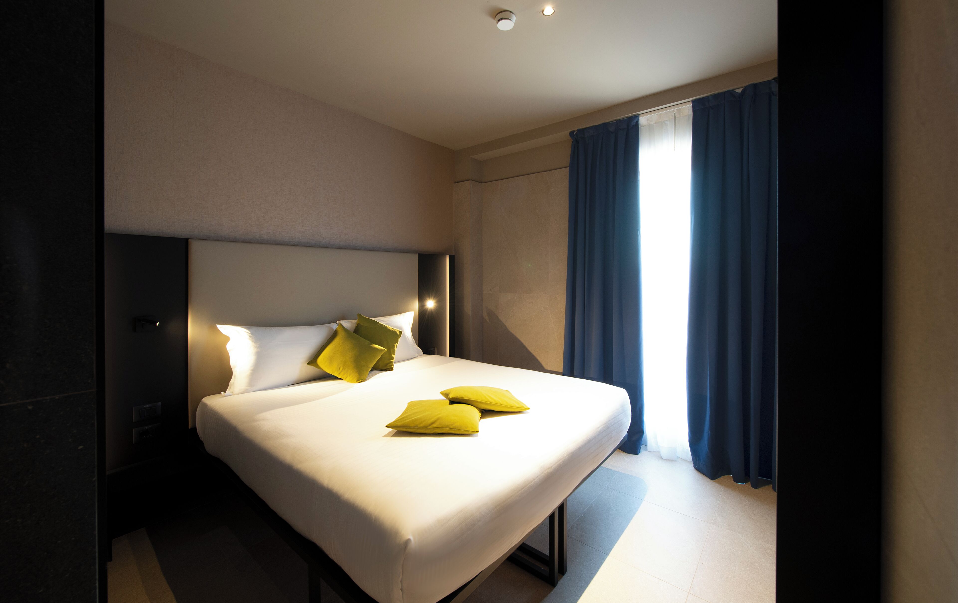 A hotel room with a large bed, a headboard, a nightstand, and a window with curtains.