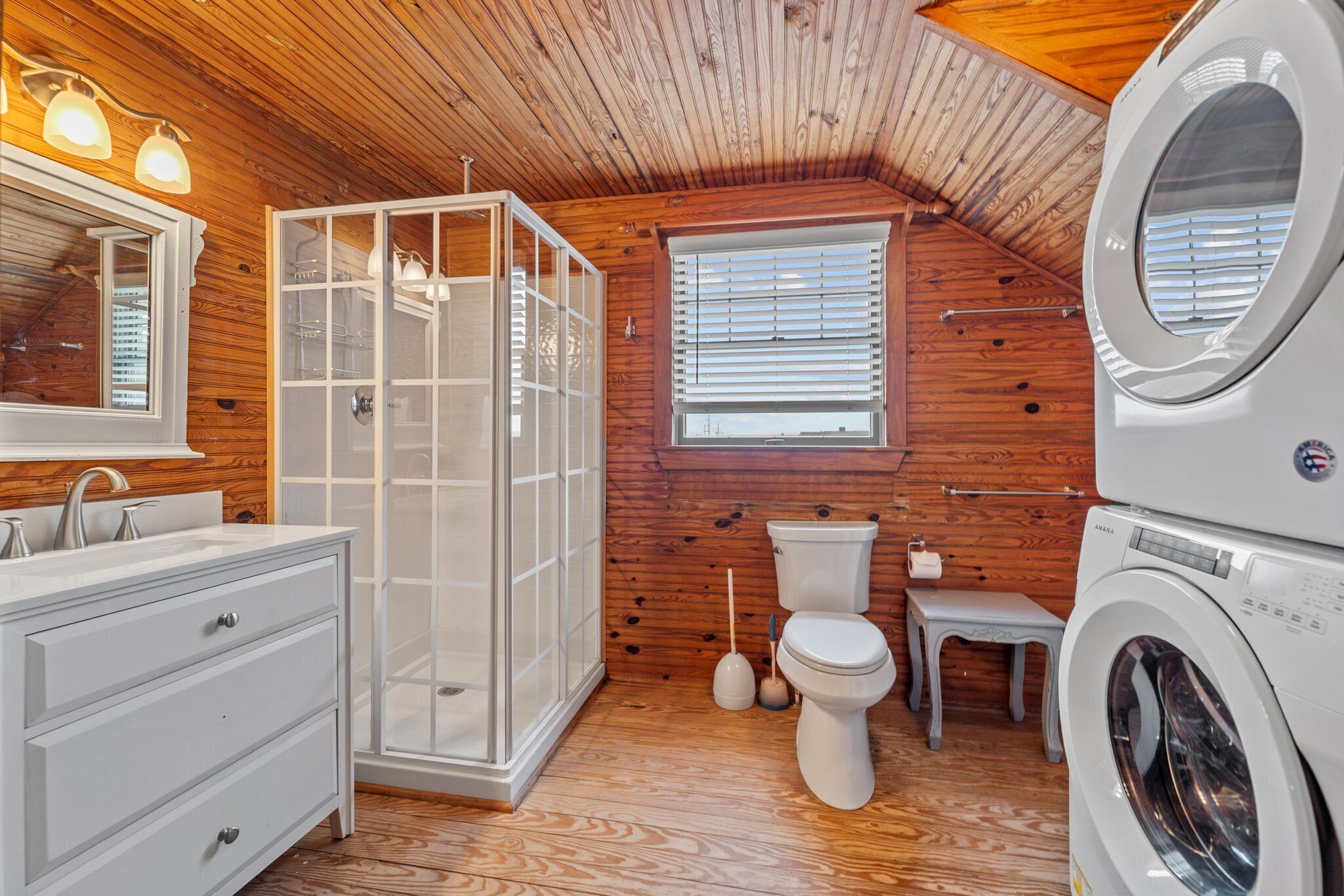 Une salle de bain compacte aux murs lambrissés, comprenant un espace douche, des toilettes, un lavabo et un lave-linge.