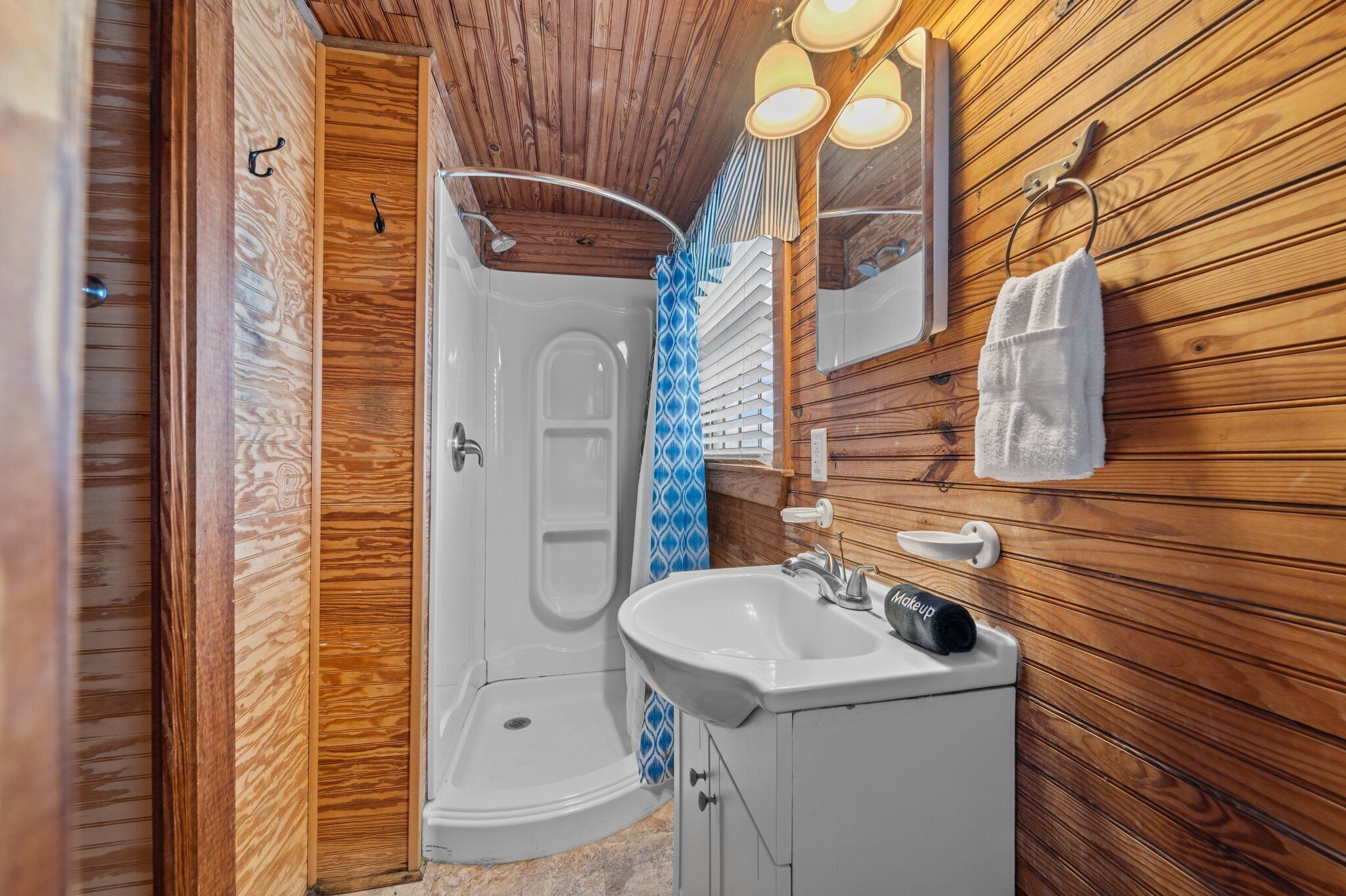 Une salle de bain aux murs lambrissés, avec un lavabo blanc, un miroir et une douche.