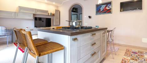 Una cocina moderna con una isla central, taburetes de bar, una mesa de comedor y una televisión.
