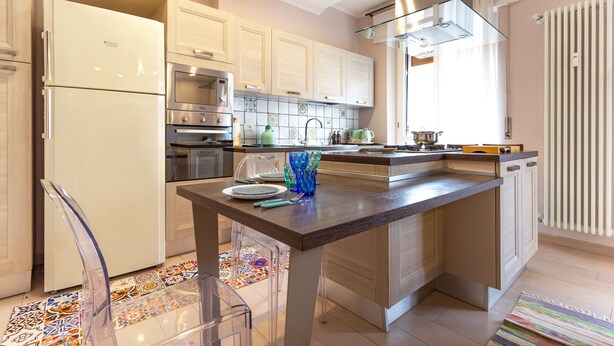 A modern kitchen with white cabinets, stainless steel appliances, and a glass-top island. - A Casa Di Giò by TuscanyWeGo (Livorno)