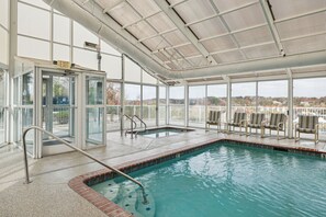 An indoor swimming pool with clear glass walls, a roofed area with chairs, and an exit sign.