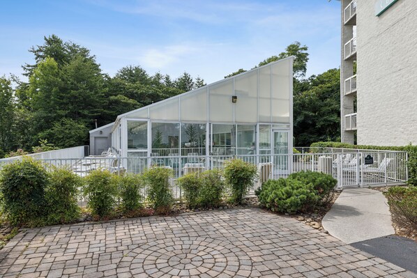 A modern building with a glass facade, surrounded by a white fence and greenery.
