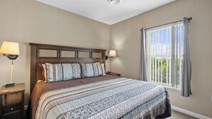 Une chambre à coucher avec un grand lit, deux tables de chevet, une fenêtre avec des rideaux et une vue sur la verdure.
