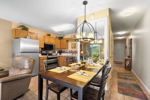 A modern kitchen with wooden cabinets, a stainless steel refrigerator, and a dining area with a table set for four. - Top Floor, Scenic Mtn View, Walk-in Shower (Pigeon Forge)