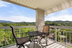 Un balcon avec une table et des chaises, donnant sur un paysage boisé.
