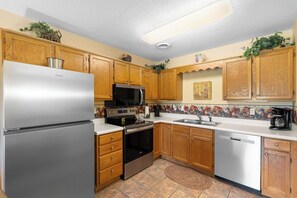 A kitchen with wooden cabinets, a stainless steel refrigerator, a microwave, a stove, and a dishwasher.