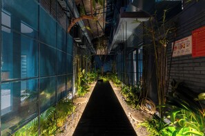 A narrow indoor corridor with a central pathway flanked by dense foliage and a mesh wall on one side. - AnNam Village 2 (Vũng Tàu)