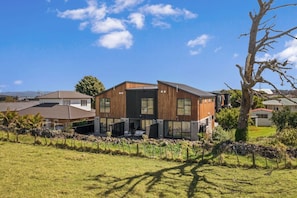 Uma casa moderna de dois andares com um amplo jardim frontal, um muro de pedra e uma árvore.