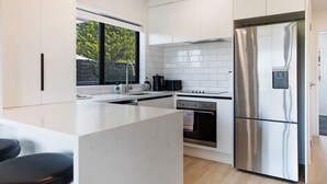 Una cocina moderna con armarios blancos, un refrigerador de acero inoxidable, un horno empotrado y un amplio ventanal.