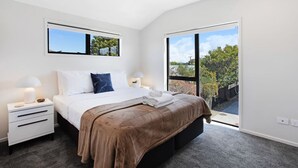 Un dormitorio moderno con una cama grande, dos mesitas de noche y una pequeña mesa auxiliar, y vistas a zonas verdes a través de un ventanal corredero.