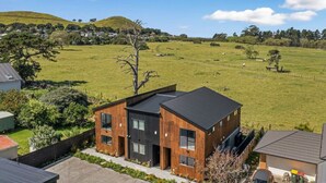 Una casa moderna de dos pisos con ventanas amplias y techo plano, rodeada por un campo verde exuberante y un paisaje montañoso al fondo.