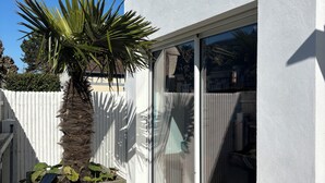 A modern house with a white exterior, a large sliding glass door, and a concrete planter with a palm tree. - Vacation home, 300M BEACH (CABOURG town center)-6 people, 3 bedrooms (Cabourg)