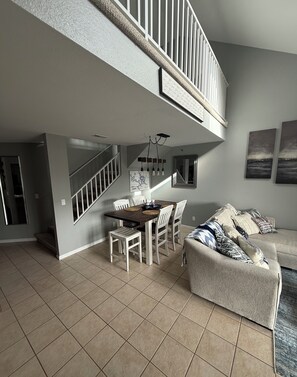 A spacious living area with a high ceiling, a dining table with chairs, a sofa, and a staircase leading to an upper level. - Lakefront Parkview Bay Condo/Amazing Views/Easy Access/3 Bedroom/3 Bath (Osage Beach)
