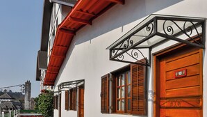 A white building with a red roof, a wooden door marked with the number 10, and a small garden area with a paved walkway. - Villaggio di Roma Suítes  (Campos do Jordao)