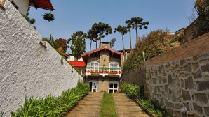 A pathway leading to a building with a red roof and a stone wall on one side. - Villaggio di Roma Suítes  (Campos do Jordao)