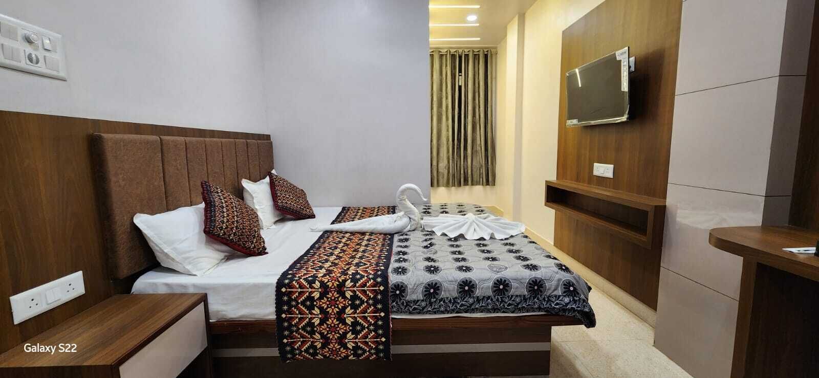 A hotel room with a Galaxy S22 bed, a TV mounted on the wall, and a wooden headboard.
