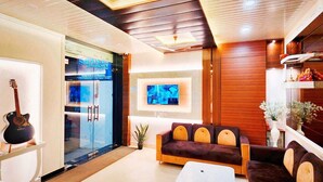 A modern living room with a glass door entrance, a sofa, a television, and a guitar. - Shanti Residency (Varanasi)