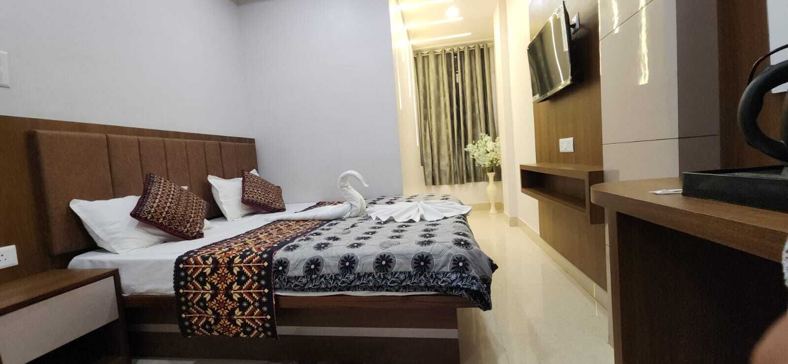 A hotel room with a bed, a TV mounted on the wall, and a desk with a chair.