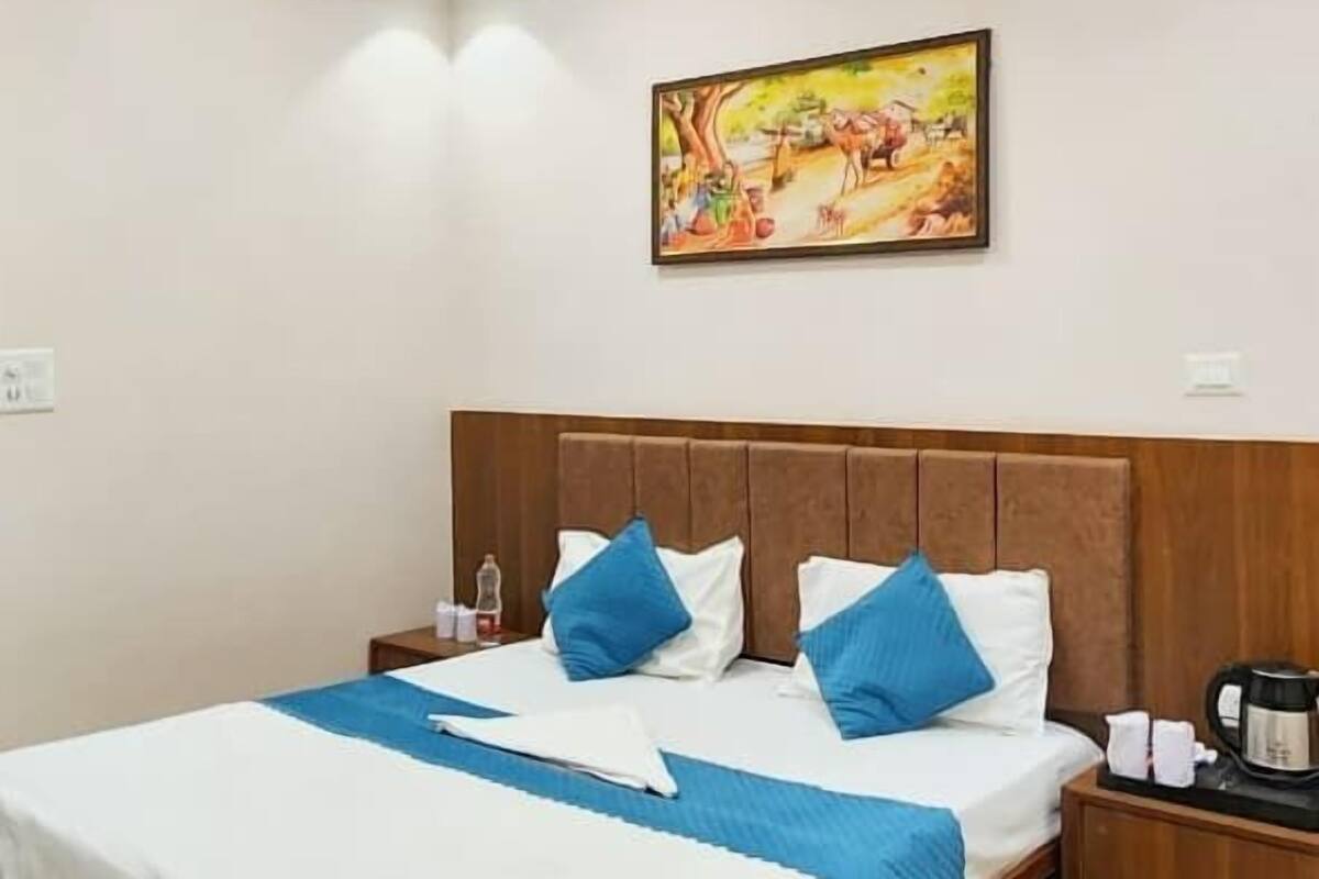 A hotel room with a large bed, a wooden headboard, a nightstand with a coffee maker, and a ceiling fan.