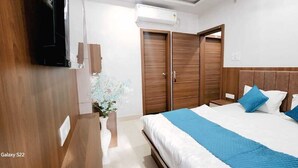 A bedroom with a bed, a nightstand, a dresser, and a TV mounted on the wall. - Shanti Residency (Varanasi)