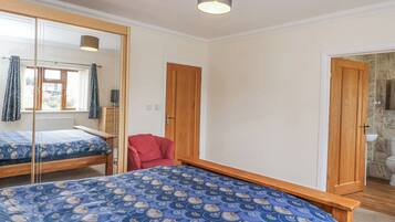 A bedroom with a bed, a mirror, a red chair, and a bathroom visible through an open door.