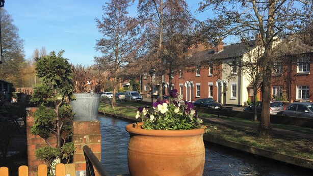 A canal with a wooden fence and a large terracotta pot with flowers.