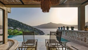 Ein Poolbereich mit zwei Liegestühlen, Meerblick und Pflanzen in Töpfen auf einem Balkon.