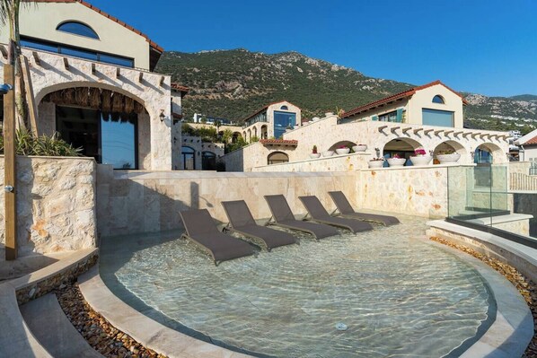 A pool area with lounge chairs, stone walls, and a mountainous backdrop.