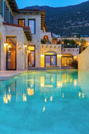 A poolside view of a building with a stone facade, multiple windows, and a staircase leading to an upper level.
