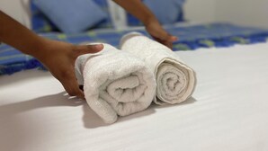 A bed with blue and white bedding, two rolled white towels, and a hand adjusting the towels. - ANCESTRAL SANTA MARTA (Santa Marta)