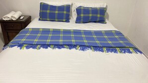A bed with a blue and green plaid blanket and pillows, a white bedspread, and a dark wooden nightstand with a rolled white towel and a remote control. - ANCESTRAL SANTA MARTA (Santa Marta)