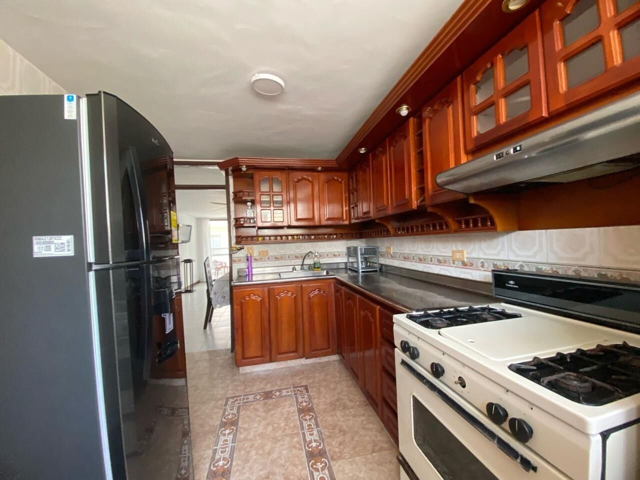 Una cocina con armarios de madera, un refrigerador de acero inoxidable, una estufa y un salpicadero de azulejos.
