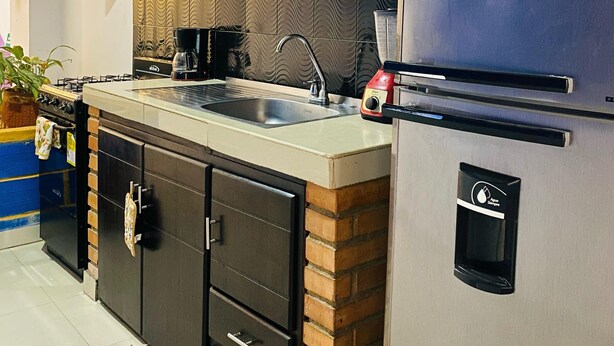 A modern kitchen with dark cabinets, a stainless steel refrigerator, a built-in oven, and a sink. - ANCESTRAL SANTA MARTA (Santa Marta)