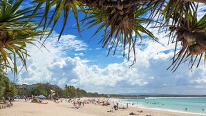 Une plage bordée de palmiers, une étendue de sable et un ciel bleu azur.
