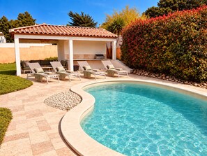 A swimming pool with lounge chairs and a covered seating area.