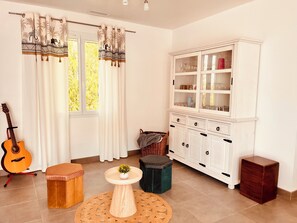 Una habitación con una guitarra, un aparador con puertas de vidrio, una mesa redonda con una planta y un taburete.
