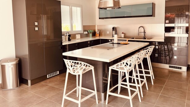 Una cocina moderna con una isla central, taburetes de bar, un refrigerador de acero inoxidable y un horno empotrado.