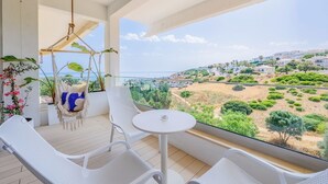 A balcony with white wicker furniture, a hanging chair, and a table. It overlooks a coastal landscape with buildings and greenery. - Ocean Studio by ENDLESS SUN  modern comfort seaview WiFi parking rooftop pool (Lagos)
