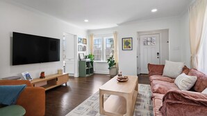Una sala de estar moderna con una televisión de pantalla plana, una mesa de centro de madera, un sofá rosa y un sillón verde.