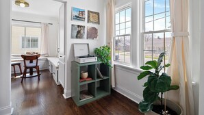 Una habitación con piso de madera, una estantería verde con una planta y una ventana con cortinas.