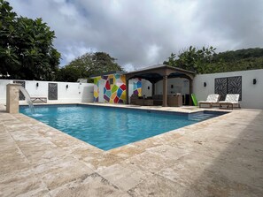 A swimming pool with a tiled deck, a covered seating area with cushions, and a colorful wall. - Sea Breeze Tunnel Hideaway 7 (Quebradillas)