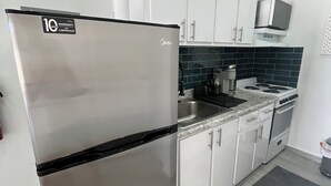 A compact kitchen with white cabinets, a stainless steel refrigerator, a microwave, and a stove. - Sea Breeze Tunnel Hideaway 7 (Quebradillas)