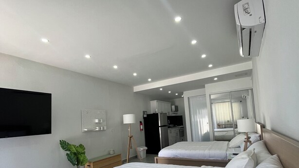 A hotel room with two beds, a TV mounted on the wall, a desk, and a kitchenette in the background. - Sea Breeze Tunnel Hideaway 7 (Quebradillas)