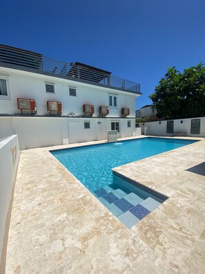 A swimming pool with a tiled deck, a white building with air conditioning units, and a tree in the background. - Sea Breeze Tunnel Hideaway 7 (Quebradillas)