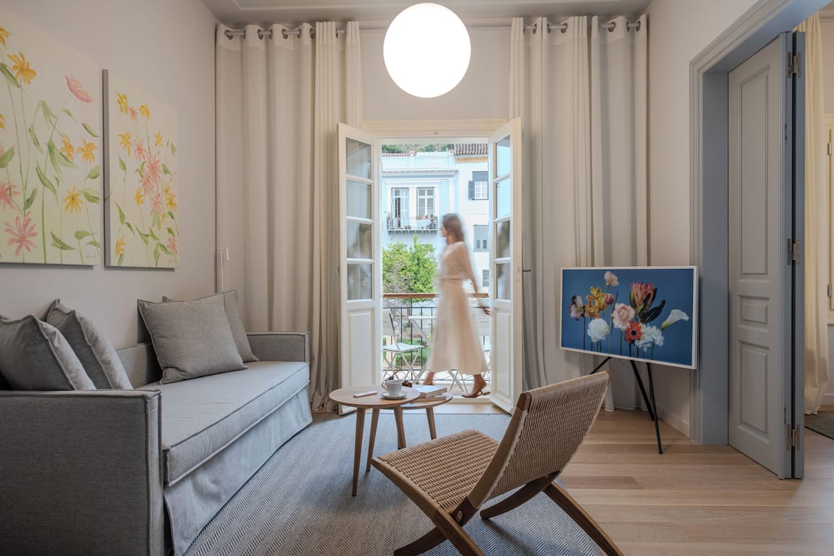 A modern living room with a sofa, a coffee table, and a chair. There is a painting on the wall, a window with curtains, and a door leading outside.