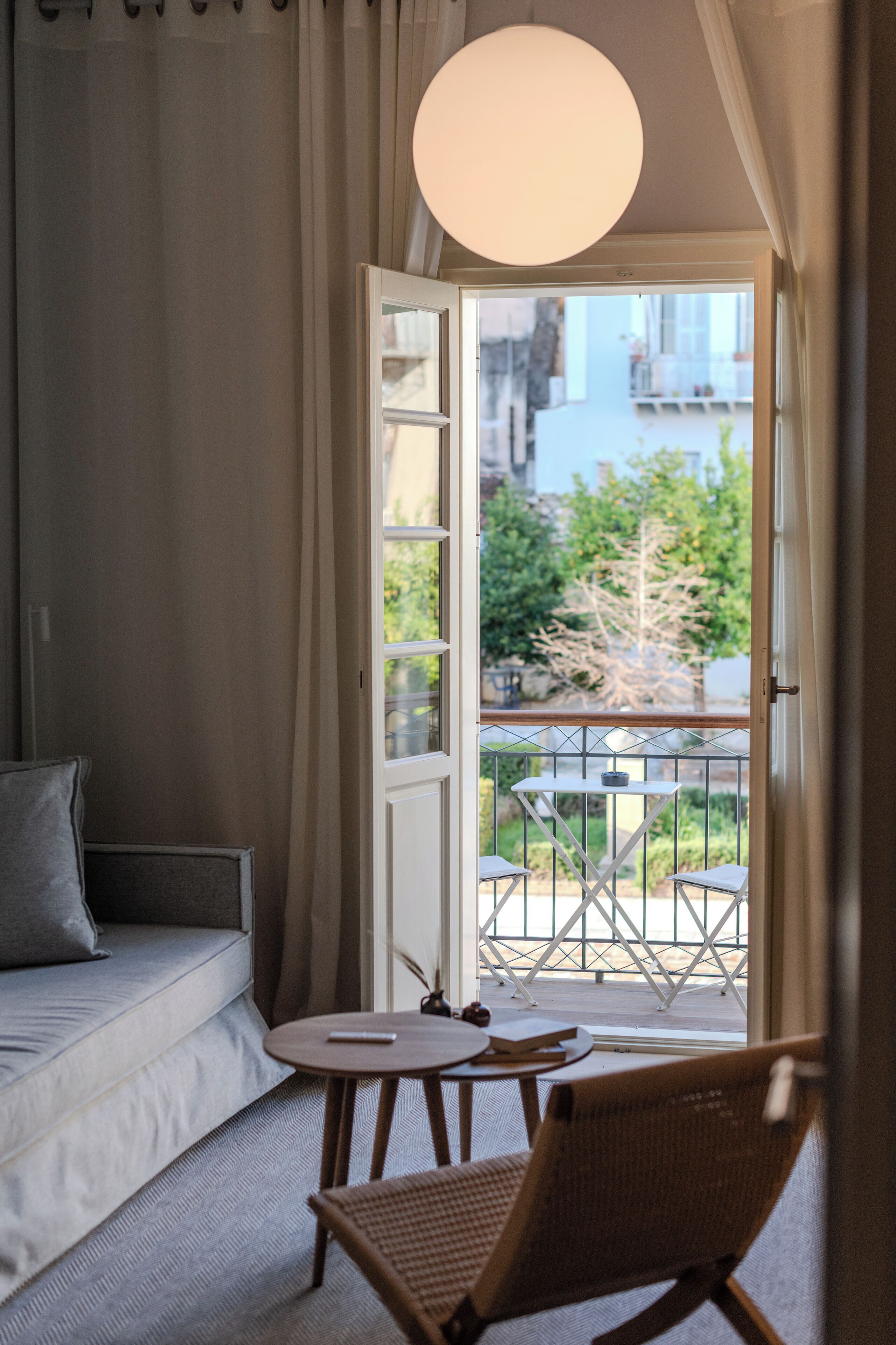 Una stanza con un divano, un tavolino, una sedia, un balcone con ringhiera e una lampada a sospensione.